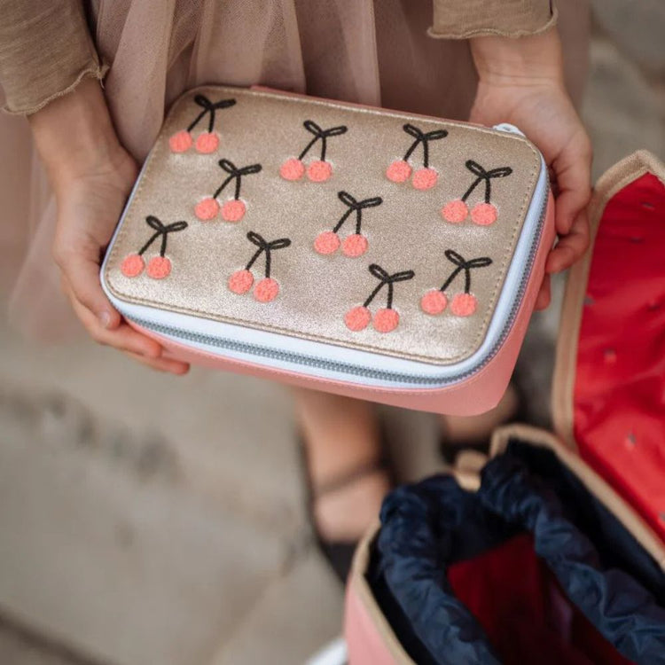 lyserødt og gyldent Cherry Pompom Penalhus fra Jeune Premier der er på vej ned i en skoletaske